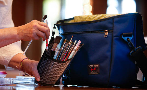 A person removing a pencil from a Pen Tool Wrap filled with art brushes and tools.